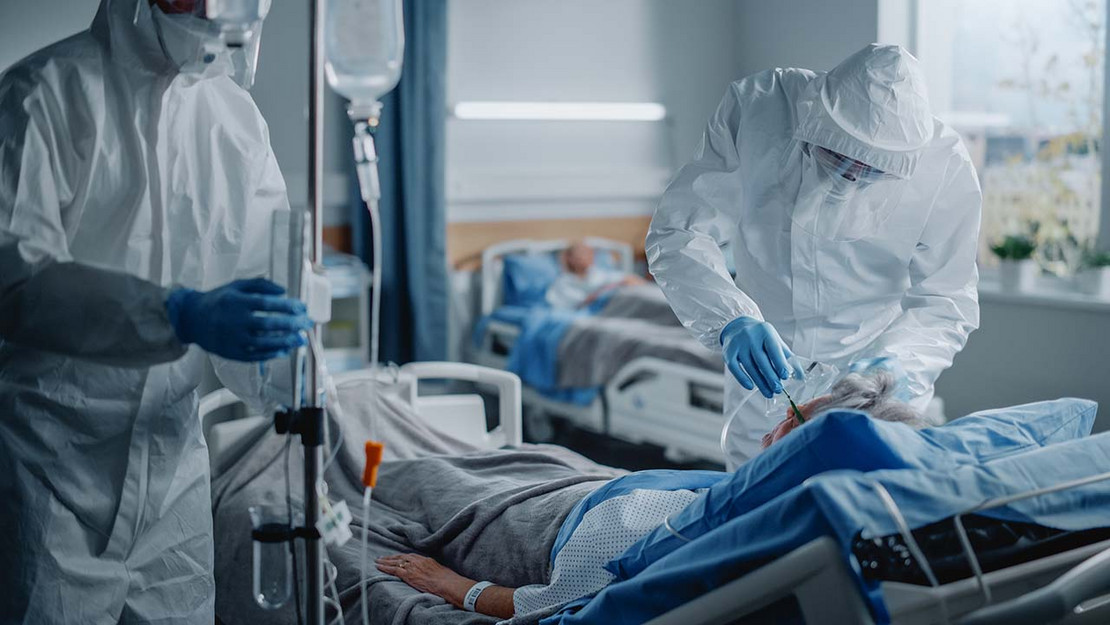 Mediziner im Schutzanzug behandeln Patientin auf der Intensivstation. 