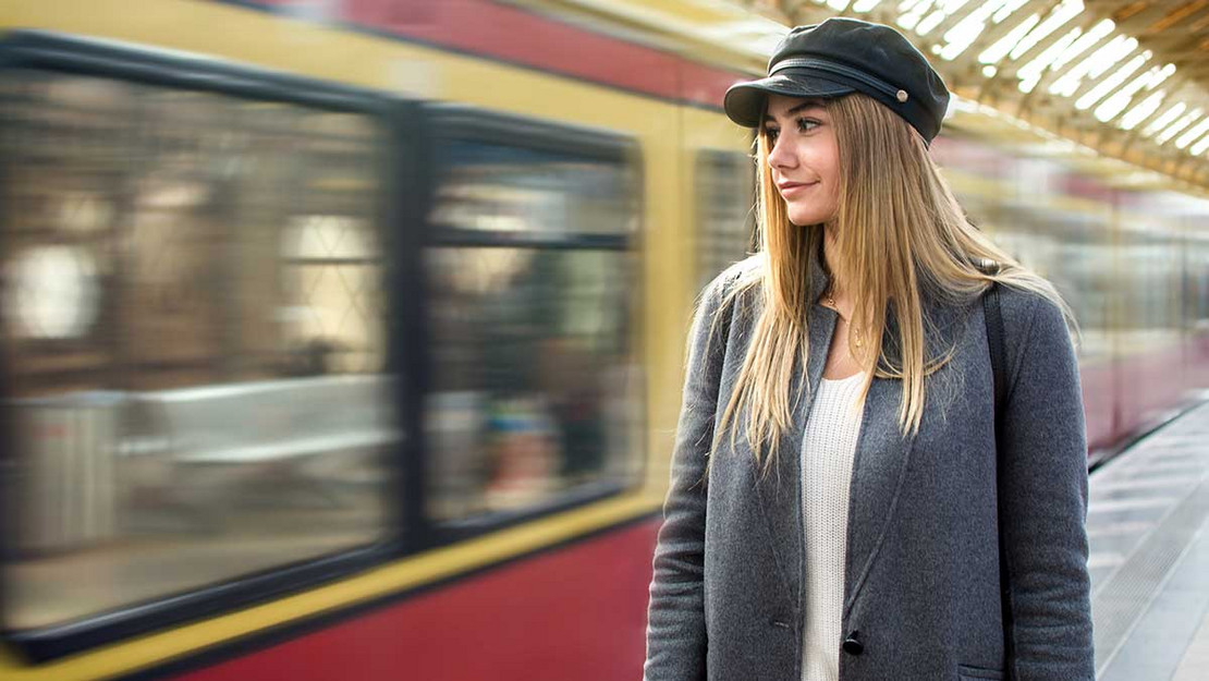 Frau steht am Bahnhof vor einer einfahrenden S-Bahn. 